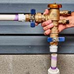 Hand holding a backflow prevention valve with blue and brass fittings, highlighting plumbing safety measures crucial for preventing water contamination.