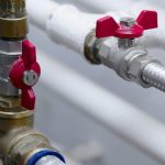 Red valve handles on plumbing pipes, illustrating essential components for residential plumbing maintenance and repair.