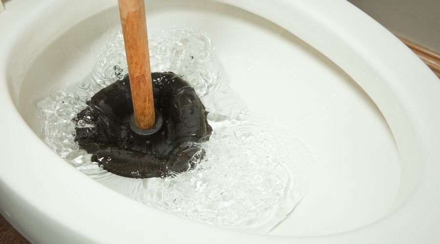 Plunger in toilet bowl with water, illustrating clogged toilet issue related to plumbing maintenance tips.