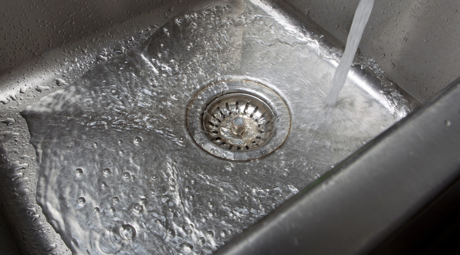 Stainless steel sink with flowing water, illustrating the importance of drain maintenance and signs of potential clogs.